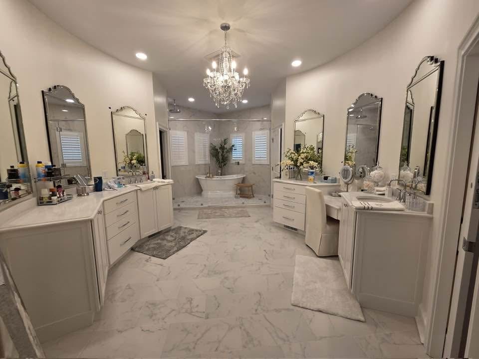 Spacious bathroom with dual vanities, marble floors, a central bathtub, three mirrors on each side, a chandelier installed by a professional electrician, and decorative plants.